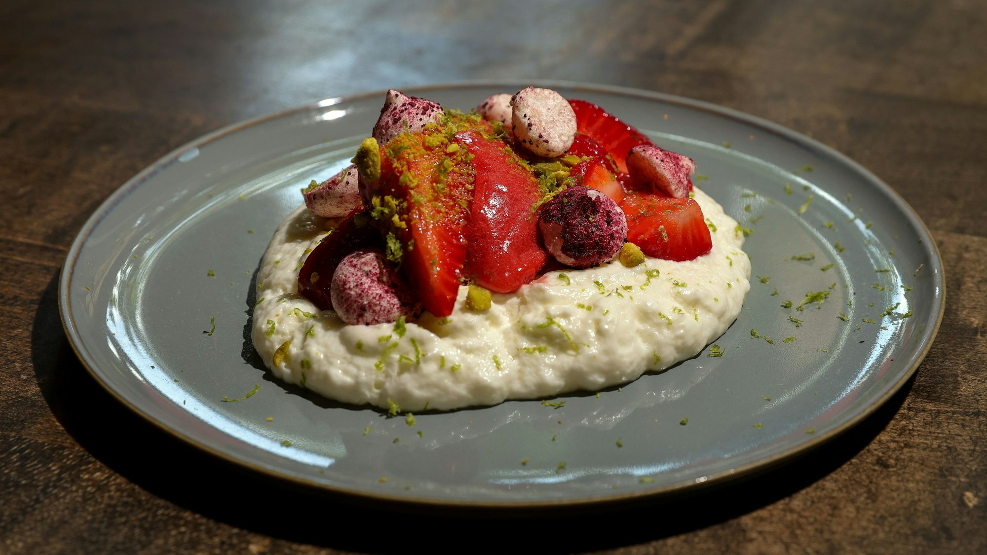 Marinierte Erdbeeren mit Joghurtschaum, Erdbeer- Sorbet und Baiser mit Hibiskus & gerösteten Pistazien, auf einem Teller angerichtet