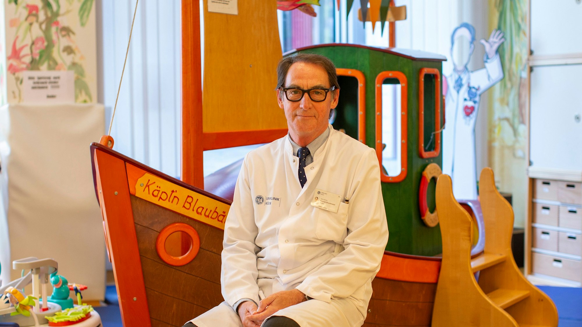 Professor Konrad Brockmeier sitzt vor einem Holzspielschiff auf seiner Kinderstation