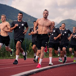Eine Gruppe von Männern läuft, im Hintergrund die Alpen.&nbsp;