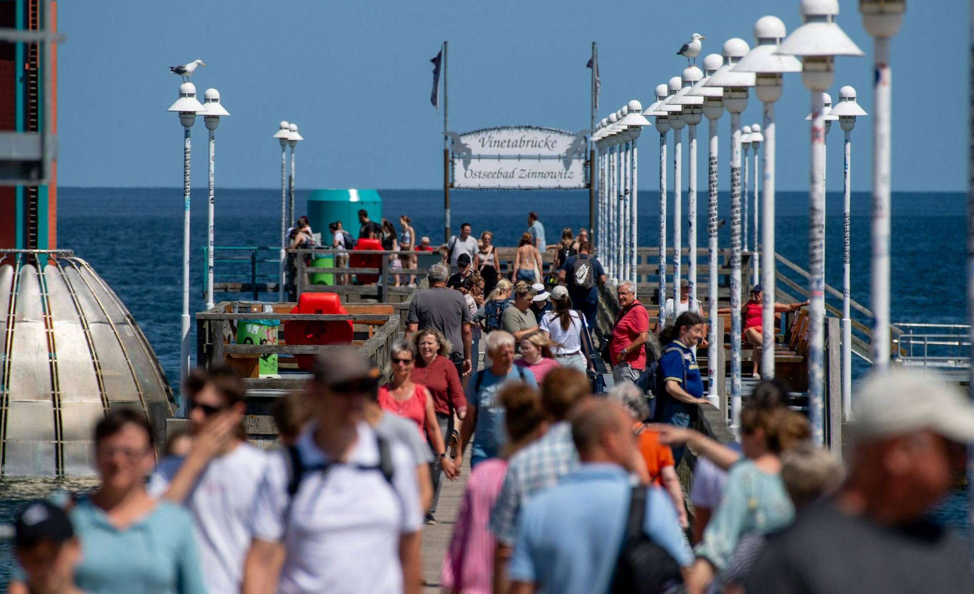Touristen und Touristinnen gehen bei sonnigem Wetter über die Seebrücke am Strand der Insel Usedom.