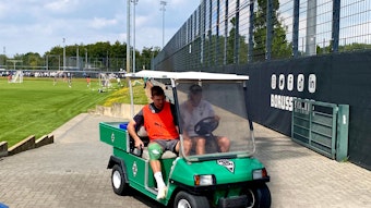 Christoph Kramer (l.) wird am 21. Juli 2023 beim Training von Borussia Mönchengladbach mit einem Golf-Kart vom Platz gefahren. Der Weltmeister hat sich am rechten Knie verletzt, das dick bandagiert ist.