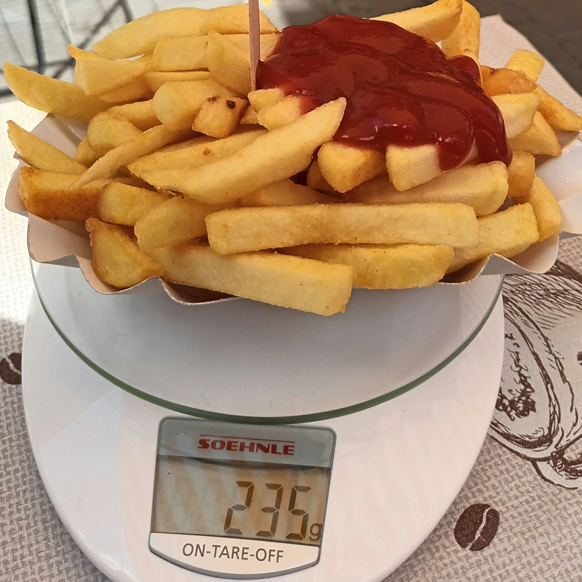 Eine Portion Pommes mit Ketchup stehen auf einer Küchenwaage, die 235 Gramm zeigt.