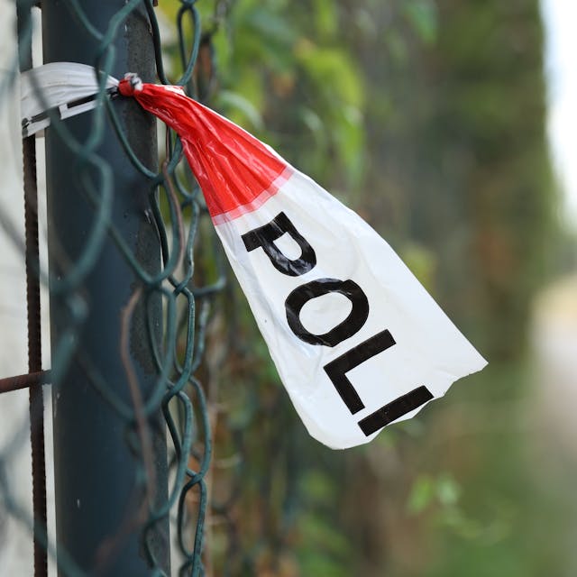 Nahe einem Tatort hängt Polizeiabsperrband an einem Zaun (Symbolbild)

