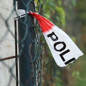 Nahe einem Tatort hängt Polizeiabsperrband an einem Zaun (Symbolbild)

