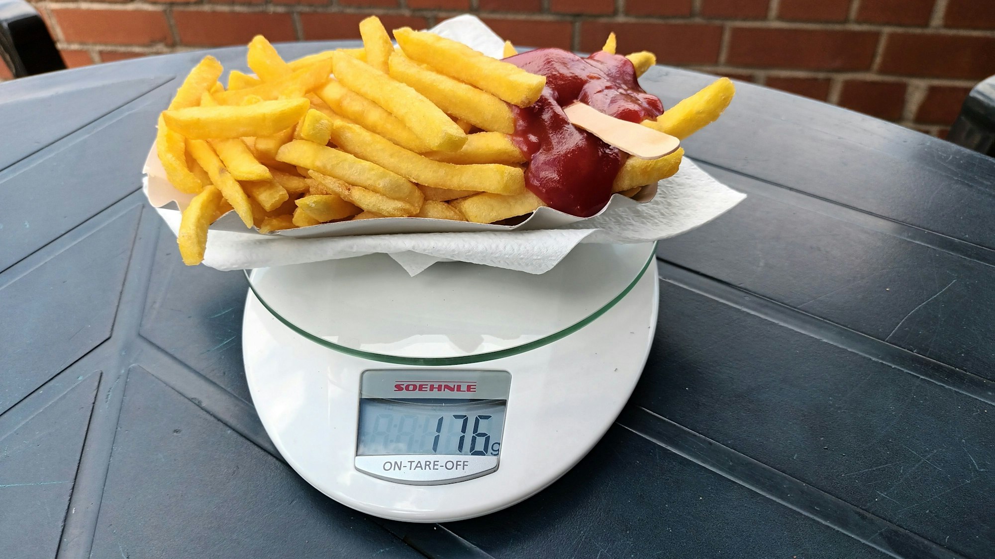 Ein Schälchen Pommes mit Ketchup und einer Holzgabel steht auf einer Küchenwaage, die 176 Gramm anzeigt.