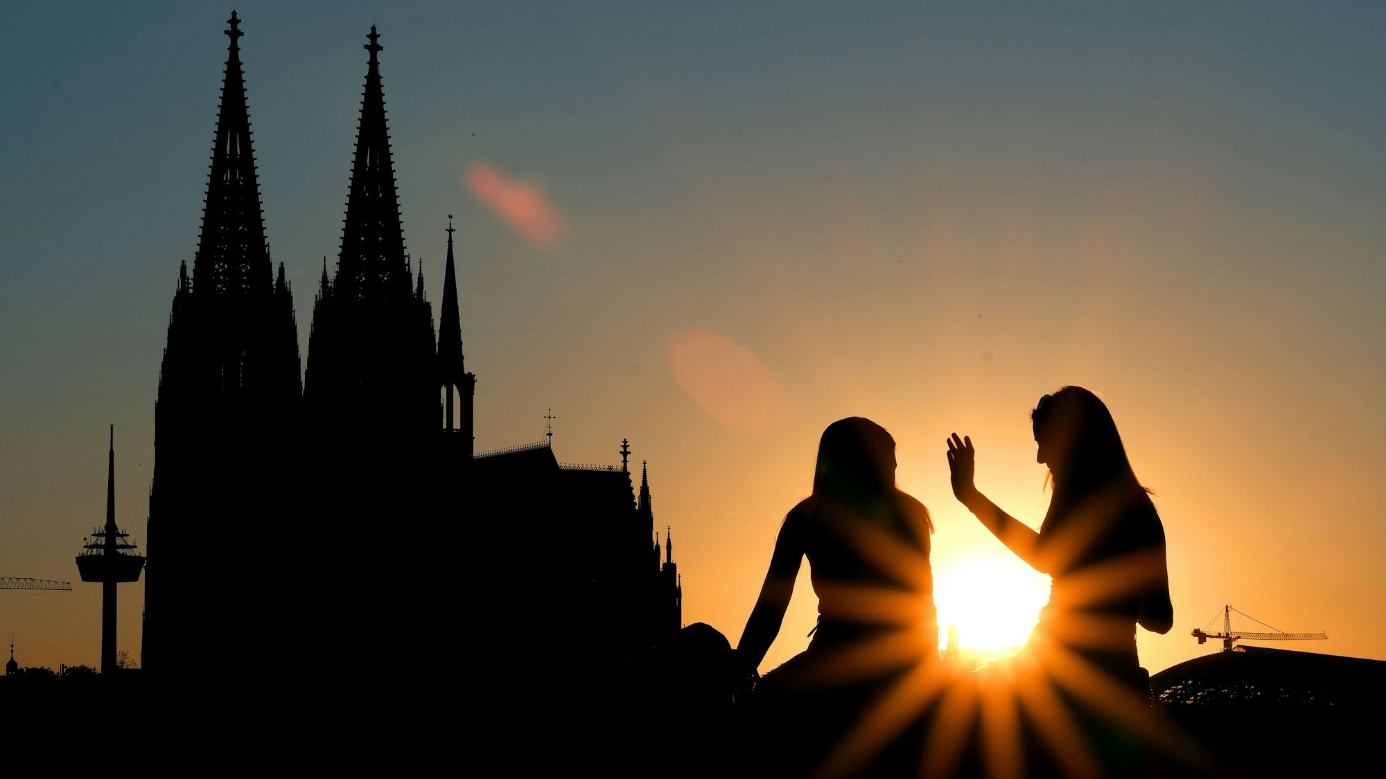 Zwei Frauen sitzen im Sonnenuntergang am Rheinboulevard vor dem Dom. (zu dpa «Drei Viertel der Deutschen finden Kirchensteuer nicht zeitgemäß»)