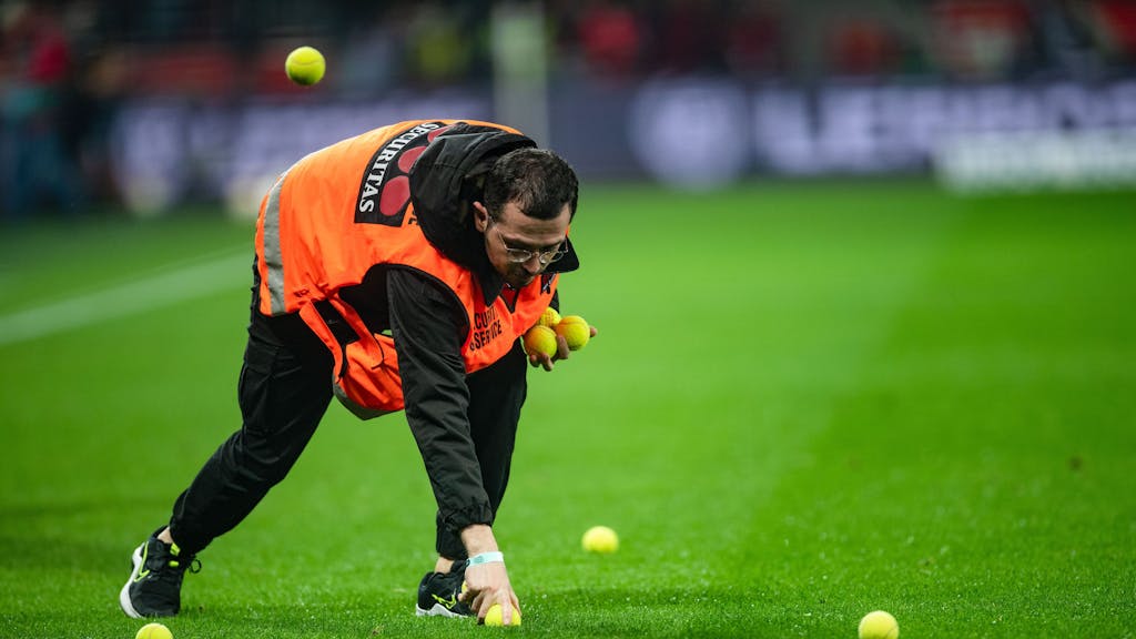 Ein Ordner sammelt Tennisbälle auf, die Kölner Fans auf den Rasen geworfen haben.