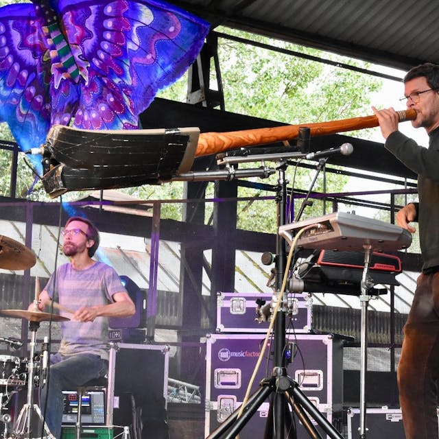 Zwei Männer stehen auf einer Bühne, einer spielt Schlagzeug, der andere ein Didgeridoo.