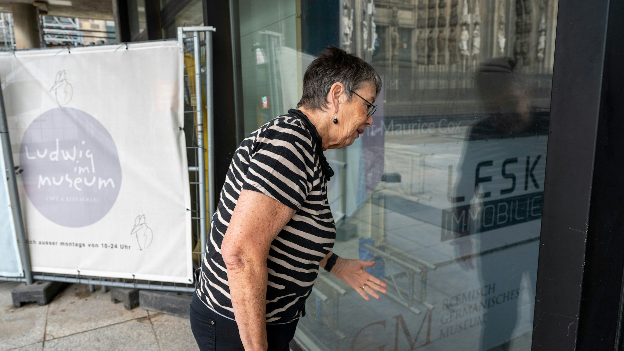 Ex-Dombaumeisterin Barbara Schock-Werner schaut durch ein Glasscheibe des Römisch-Germanischen Museums. Verschmutzte, fast blinde Scheiben erschweren den Blick auf Monumente im geschlossenen Museum