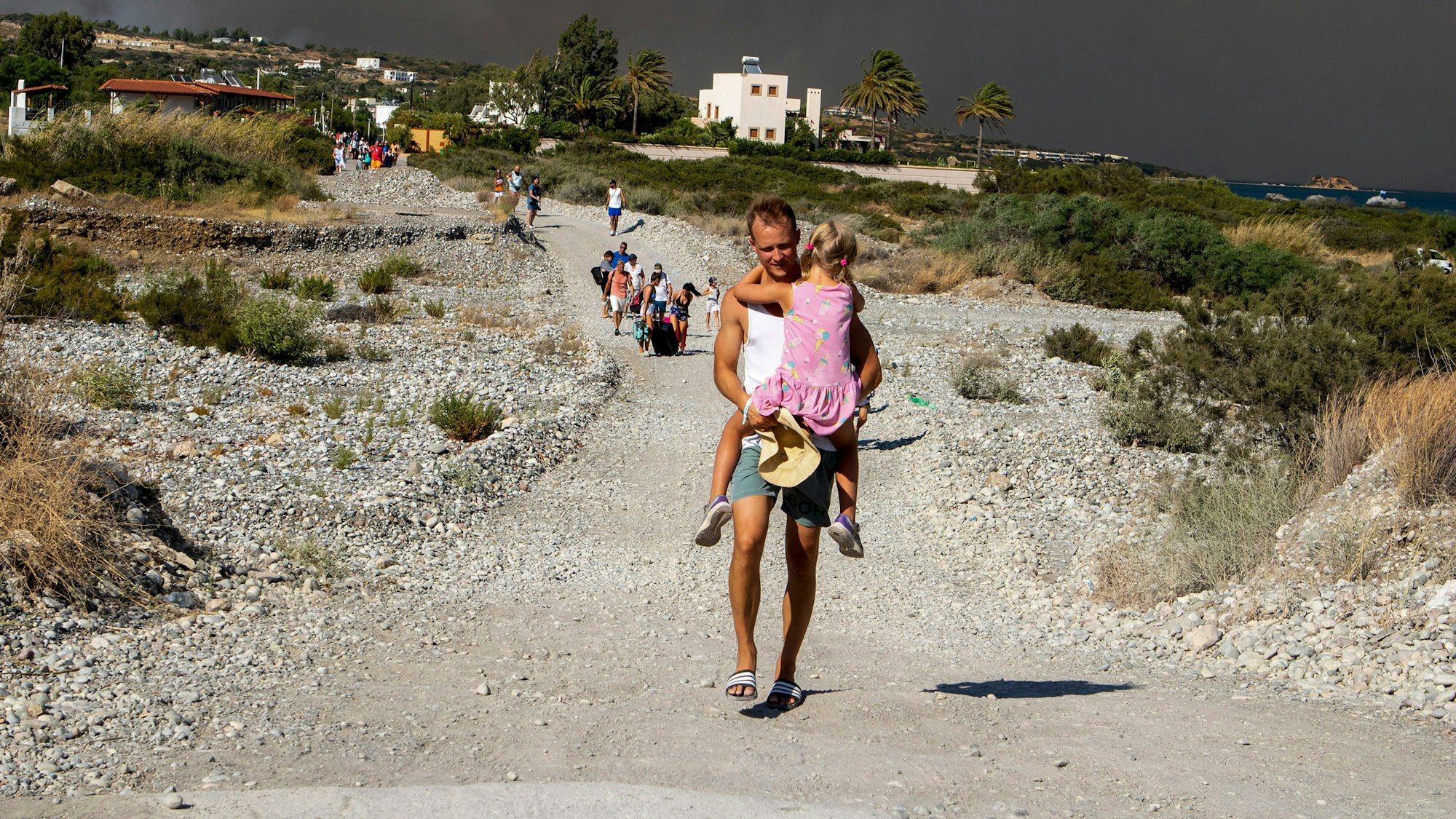 Waldbrände auf Rhodos: Ein Mann trägt ein Kind, als sie vor den Feuern fliehen. Mehrere Zehntausend Menschen sind vor den Flammen geflohen.