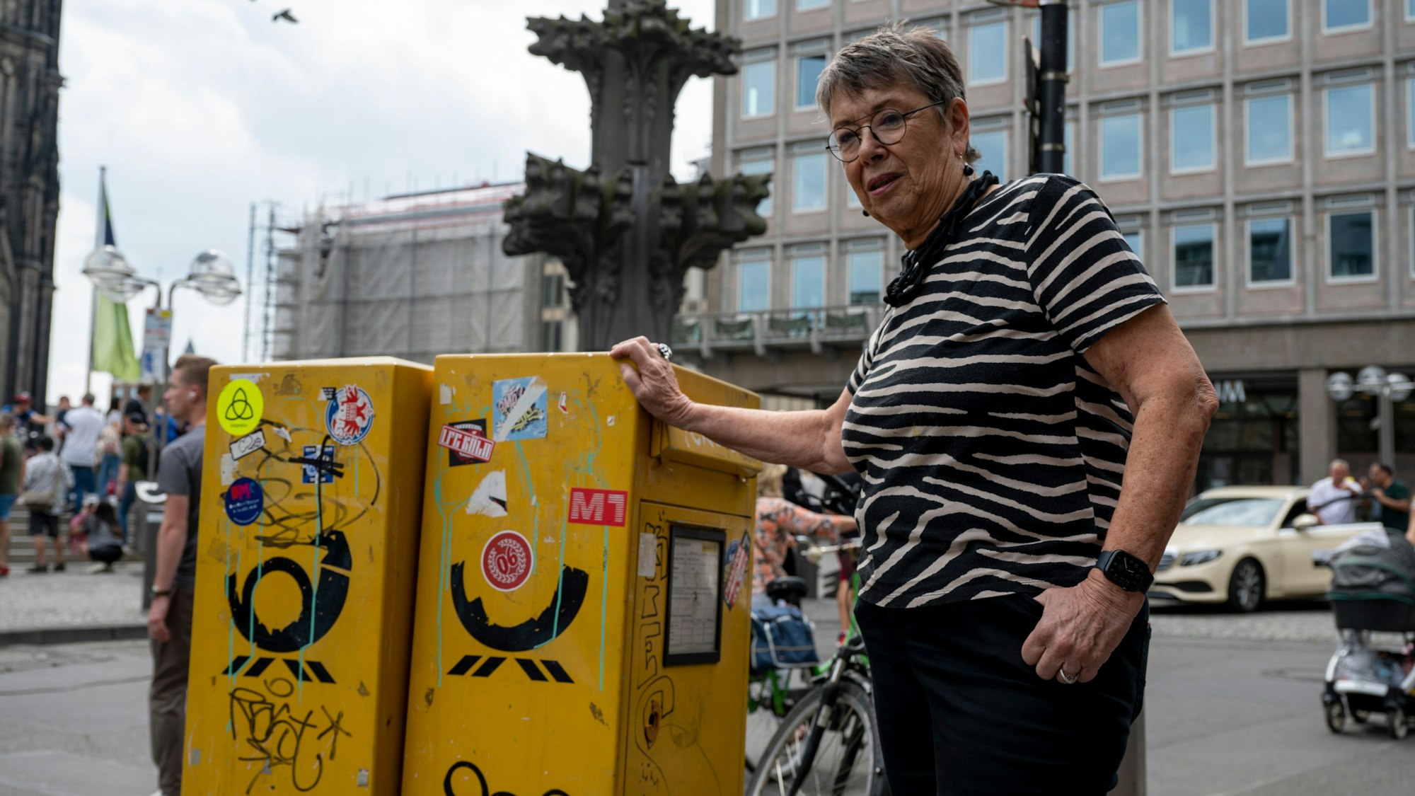 Barbara Schock-Werner steht vor zwei verschmutzten und unansehnlichen Briefkästen auf der Domplatte, die sinnbildlich für die Verschmutzung der Domumgebung stehen, die sie kritisiert.