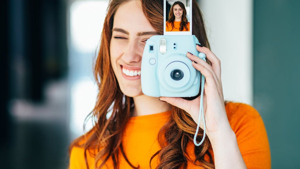 Frau hält Sofortbild-Kamera mit Bild in der Hand