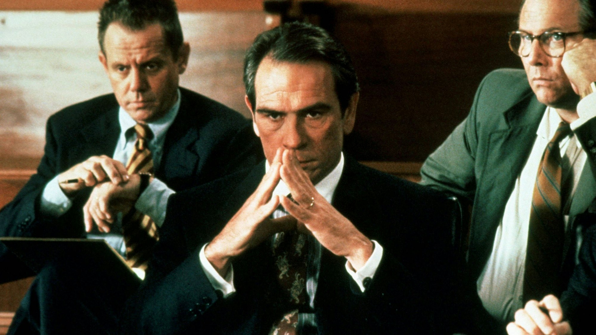 Eine Szene aus dem Film „Der Klient“ zeigt Hauptdarsteller Tommy Lee Jones bei einer Anhörung. Er schaut konzentriert mit vor dem Gesicht zusammengelegten Fingerspitze auf ein unsichtbares Gegenüber.