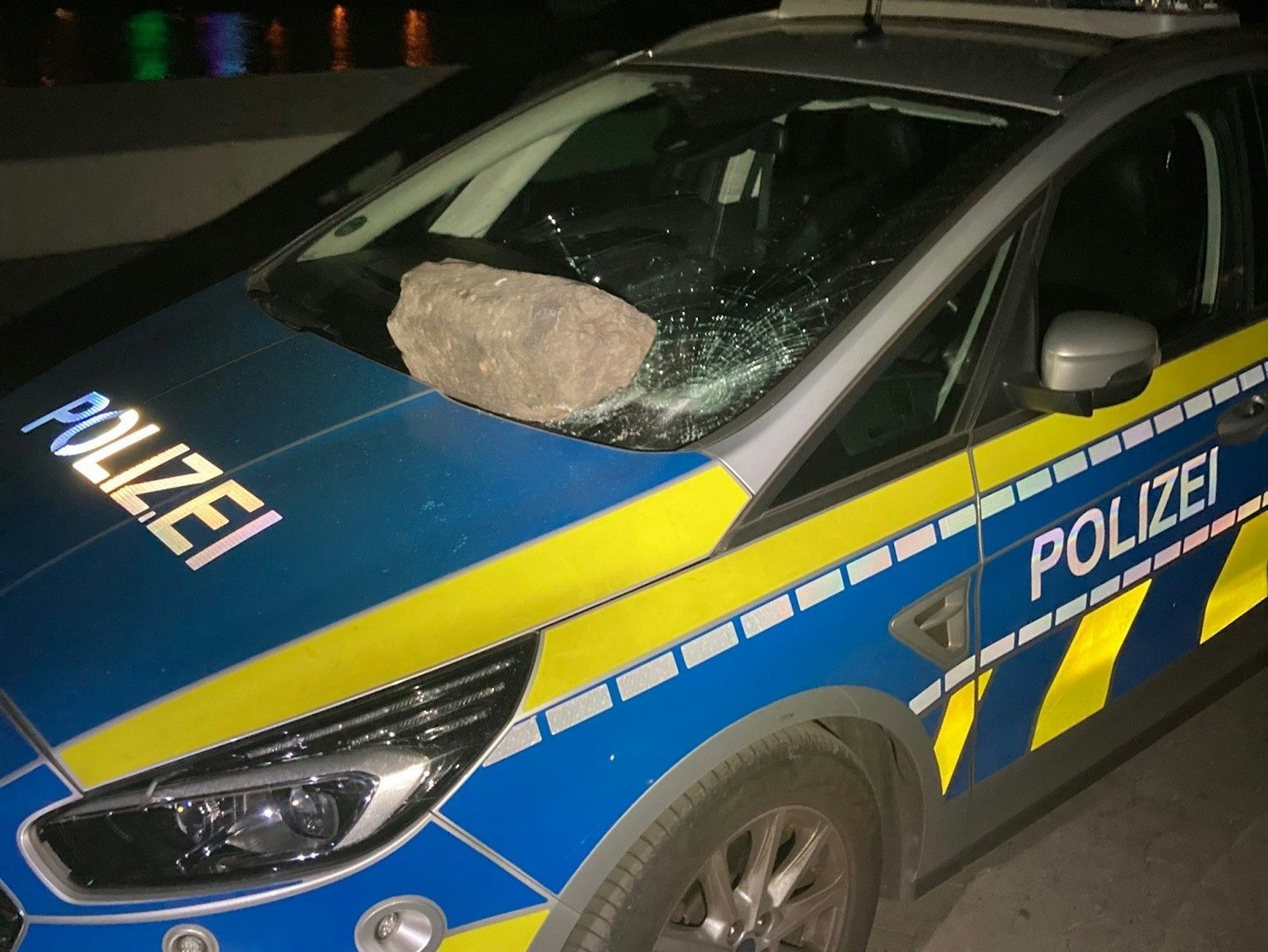Ein Stein, der auf der Frontscheibe eines Streifenwagens der Kölner Polizei liegt.