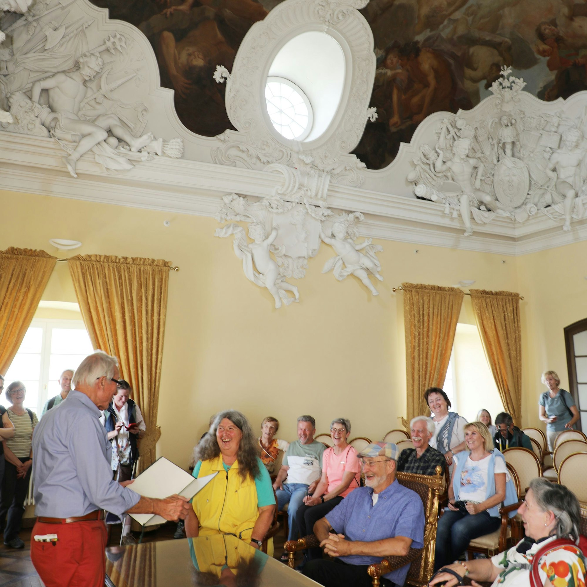 Menschen sitzen auf prunkvollen Stühlen und am Trautisch des Zanetti-Saals von Schloss Bensberg.
