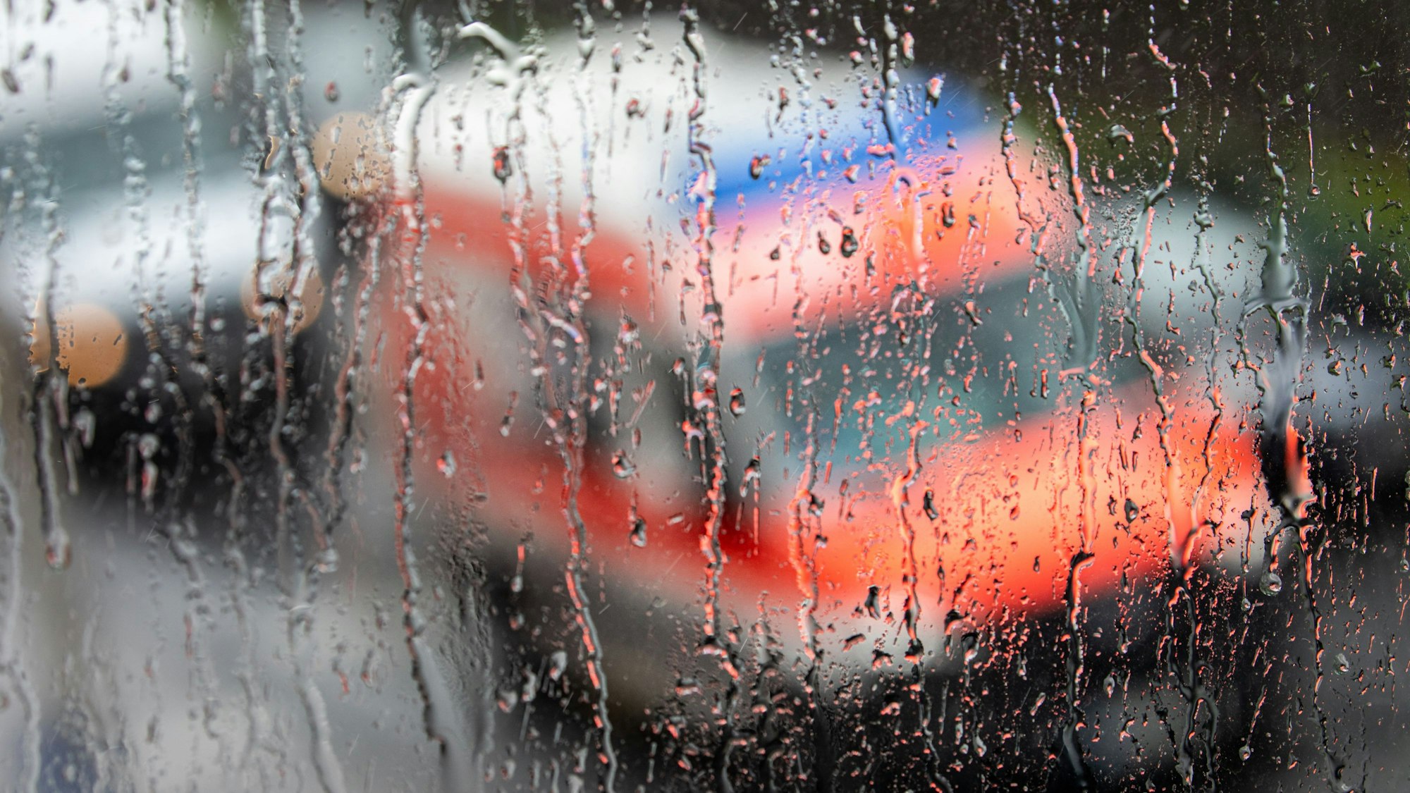 Ein Rettungswagen ist hinter einer Fensterscheibe zu sehen auf der sich  während eines Unwetters mit Gewitter und Starkregen im Ortsteil Sülz zahlreiche Regentropfen gesammelt haben.