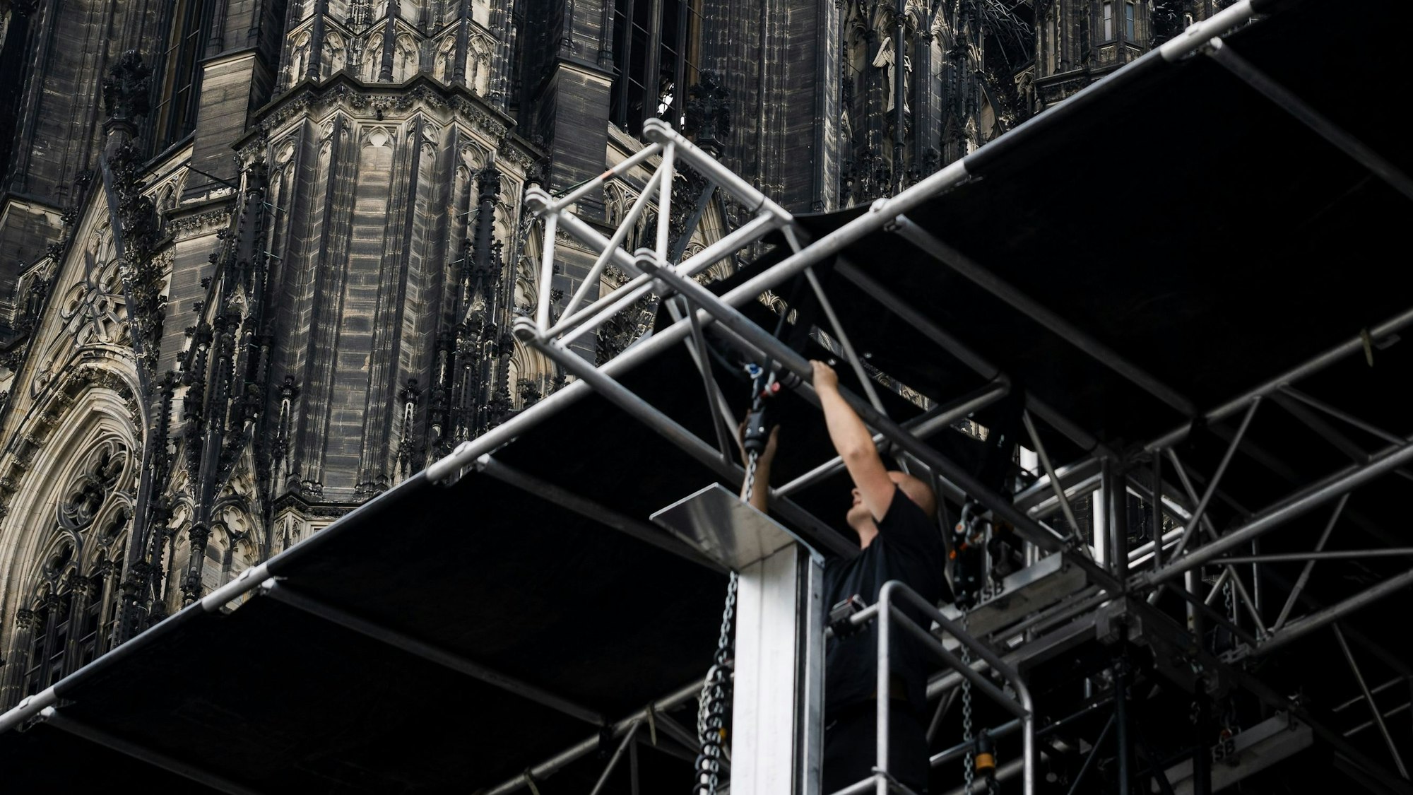Ein Arbeiter verbaut Metall am Dach der Bühne auf dem Roncalliplatz - hinter ihm der Dom.