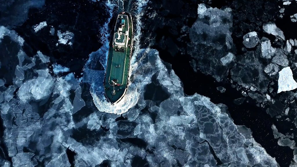 Ein Schiff fährt durch die Antarktis und schiebt Eisschollen vor sich her.