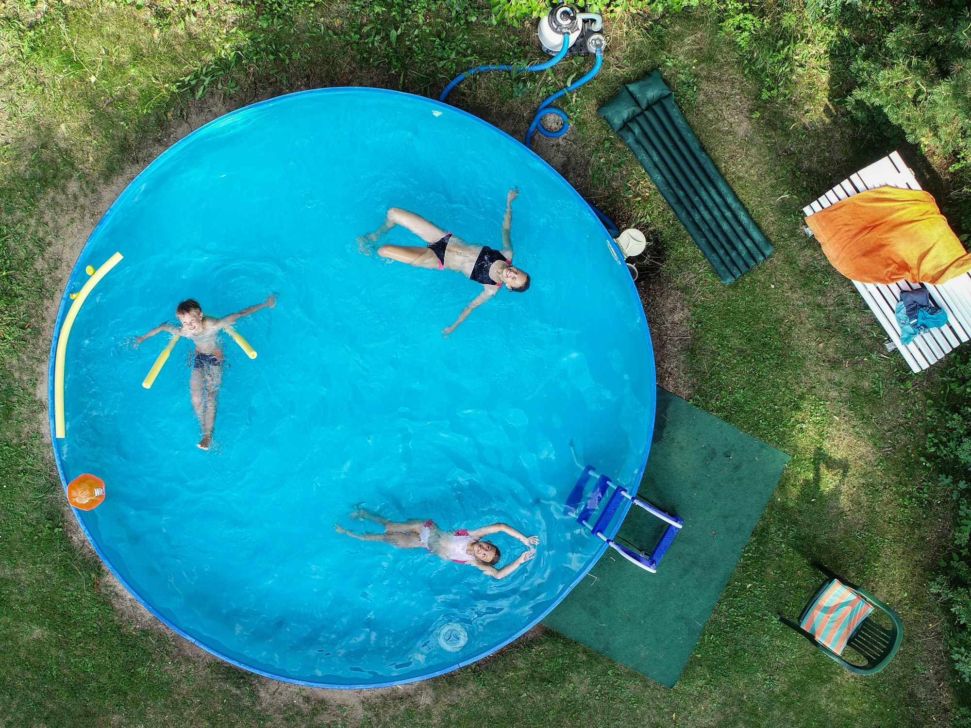 Drei Kinder in einem Swimmingpool, der in einem Garten steht.