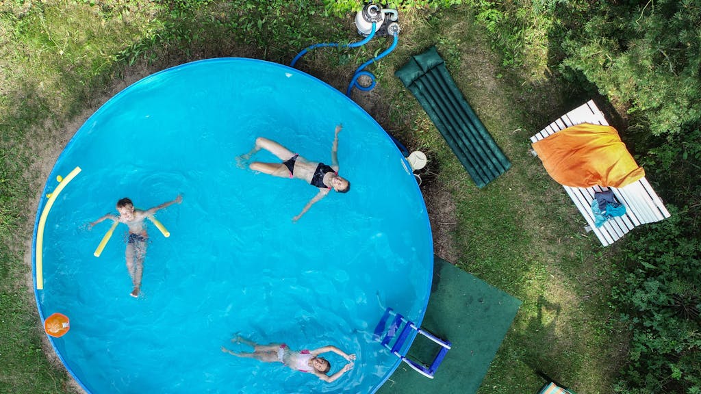 Drei Kinder in einem Swimmingpool, der in einem Garten steht.