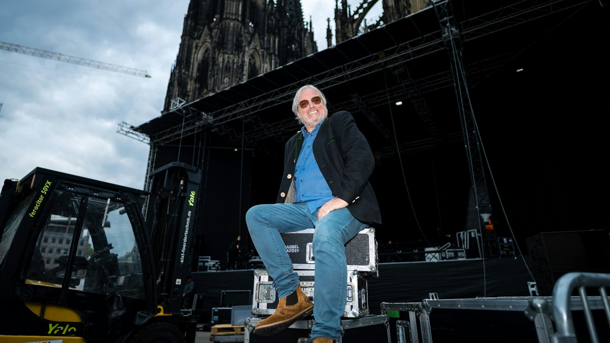 Ernst-Ludwig Hartz sitzt auf Transportboxen vor der Bühne auf dem Roncalliplatz mit Blick auf den Dom.