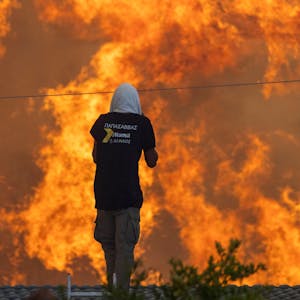 Zwei Männer stehen auf ihren Dächern vor riesigen Flammen und versuchen mit Wasserschläuchen ihre Häuser zu retten.&nbsp;