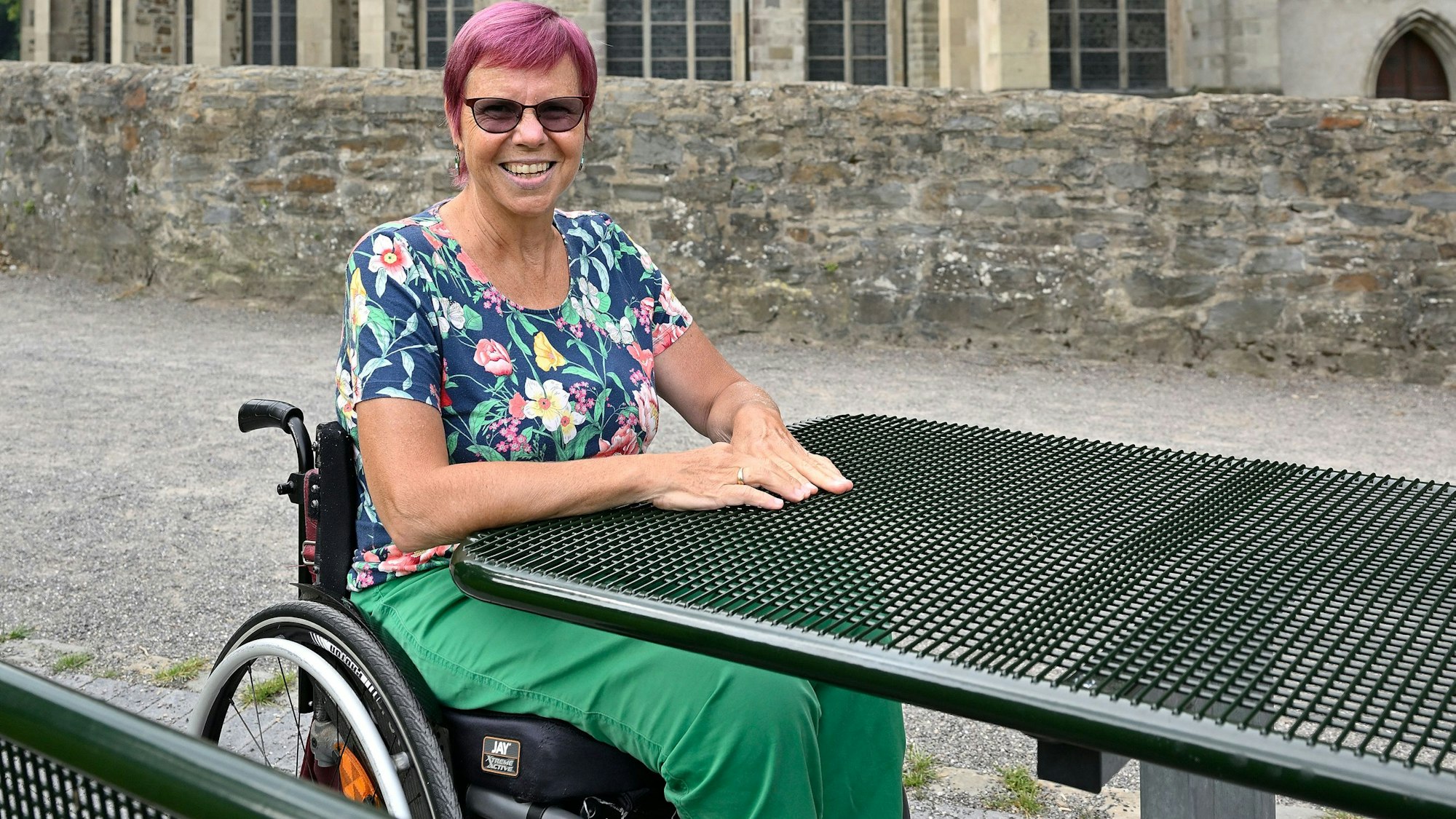 Eine Frau im Rollstuhl sitzt an einem Picknicktisch, den man mit dem Rollstuhl unterfahren kann, um bequem zu sitzen.