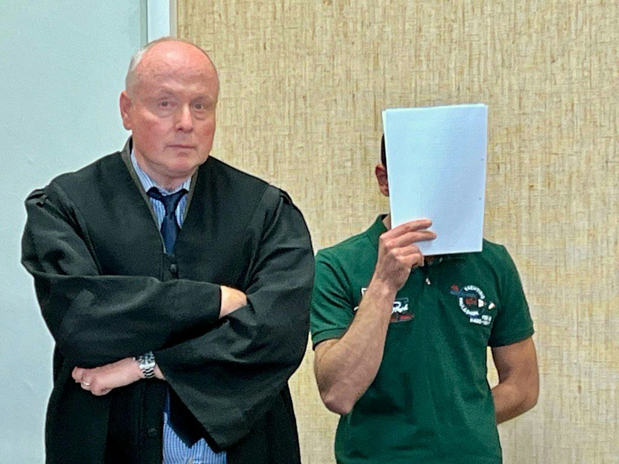 Der Beschuldigte verdeckt sein Gesicht vor den Kameras im Gerichtssaal mit einem Schreibblock.