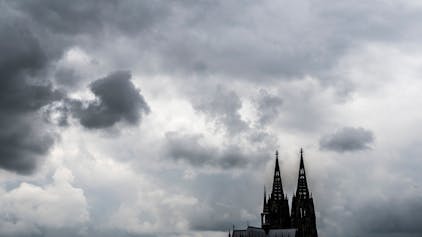 Eine leitende Mitarbeiterin des Erzbistums Köln hat ein wegweisendes Urteil gegen ihren Arbeitgeber erstritten. Unser Bild zeigt den Dom vor dunklen Wolken.