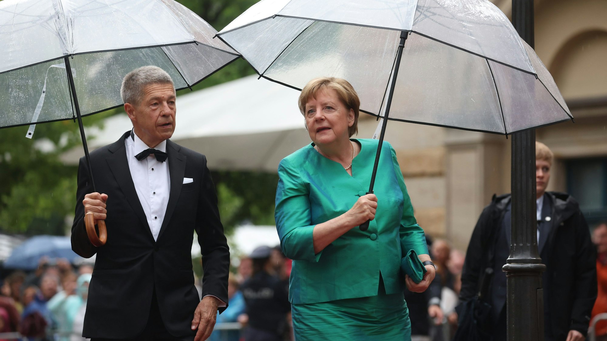 Bayern, Bayreuth: Ex-Bundeskanzlerin Angela Merkel (CDU) und Ehemann Joachim Sauer kommen mit Regenschirm zur Eröffnung der Richard-Wagner-Festspiele.