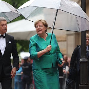 Bayern, Bayreuth: Ex-Bundeskanzlerin Angela Merkel (CDU) und Ehemann Joachim Sauer kommen mit Regenschirm zur Eröffnung der Richard-Wagner-Festspiele.