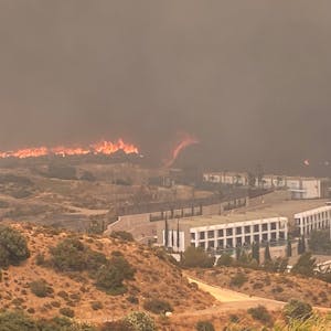 Auf dem Foto sind lodernde Flammen nahe einem Gebäude zu sehen, schwarzer Rauch breitet sich aus.