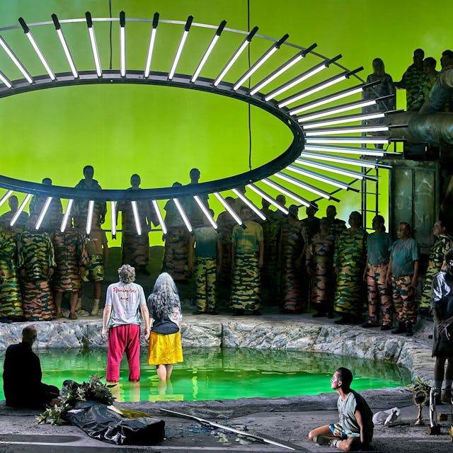 Auf der Bühne stehen Parsifal und Kundry in einer Art Teich, über ihnen ein großer Kreis mit LED-Lampen. Um sie herum stehen zahlreiche Menschen.&nbsp;