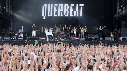 Jubelnde Menge vor einer Bühne, auf der eine Band steht. Im Hintergrund der Schrifzug „Querbeat“ zu sehen