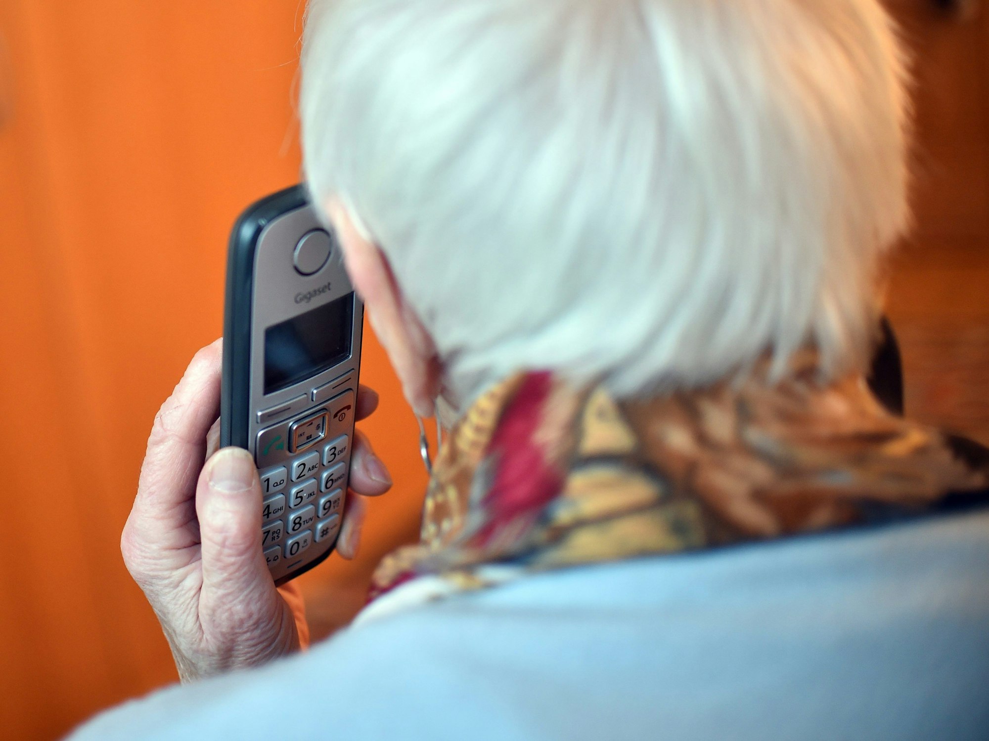 Eine Seniorin hält einen Telefonhörer an ihr Ohr.