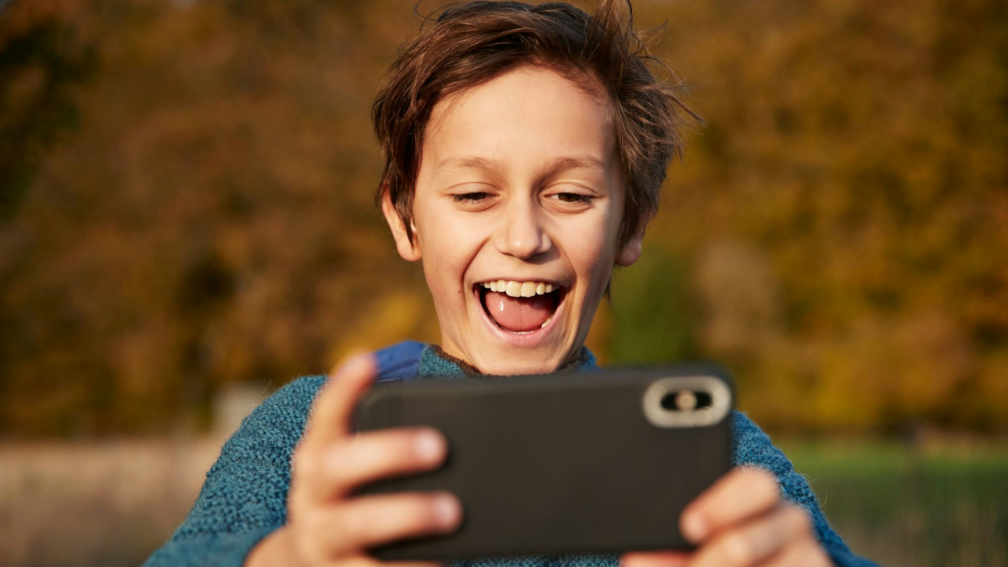 Ein Junge schaut glücklich auf sein Handy.