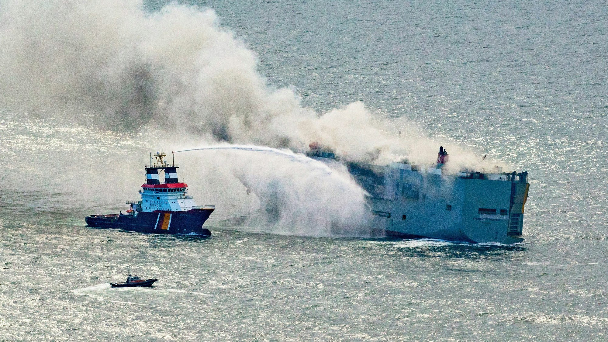 Der deutsche Notschlepper „Nordic“ versucht, den in Brand geratenen Frachter „Fremantle Highway“ in der Nordsee zu löschen. Mehrere Rettungsboote sind in der Nähe des havarierten Schiffs unterwegs.
