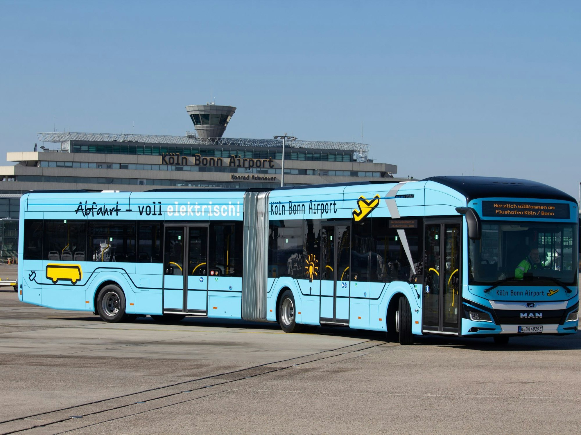 Ein Bus mit der Aufschrift „Abfahrt voll elektrisch“ steht vor einem Gebäude des Köln Bonn Airports.