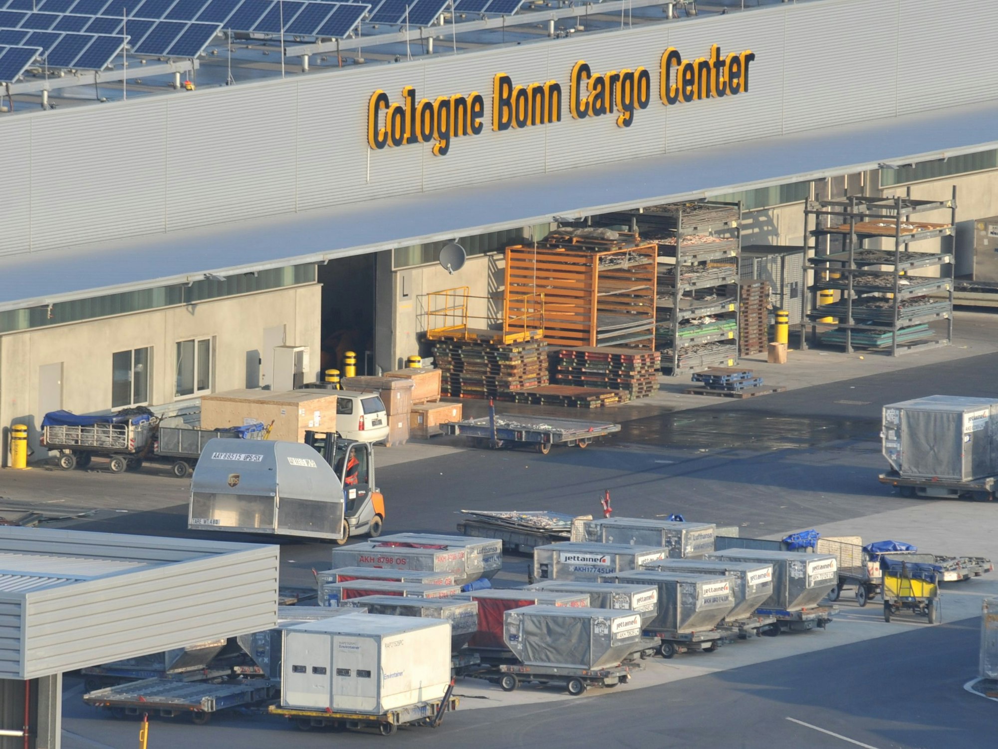 Vor einem Gebäude mit der Aufschrift „Cologne Bonn Cargo Center“ stehen zahlreiche Paletten, teilweise mit abgedeckter Fracht.