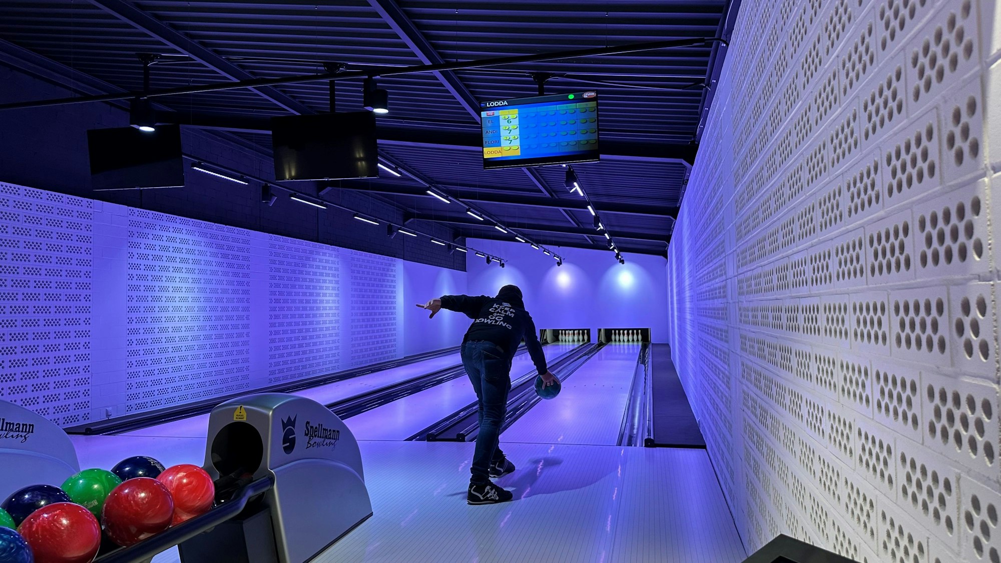 Ein Mann macht eine Bowling-typische Ausholbewegung, um eine Bowling-Kugel auf die Bahn zu befördern.