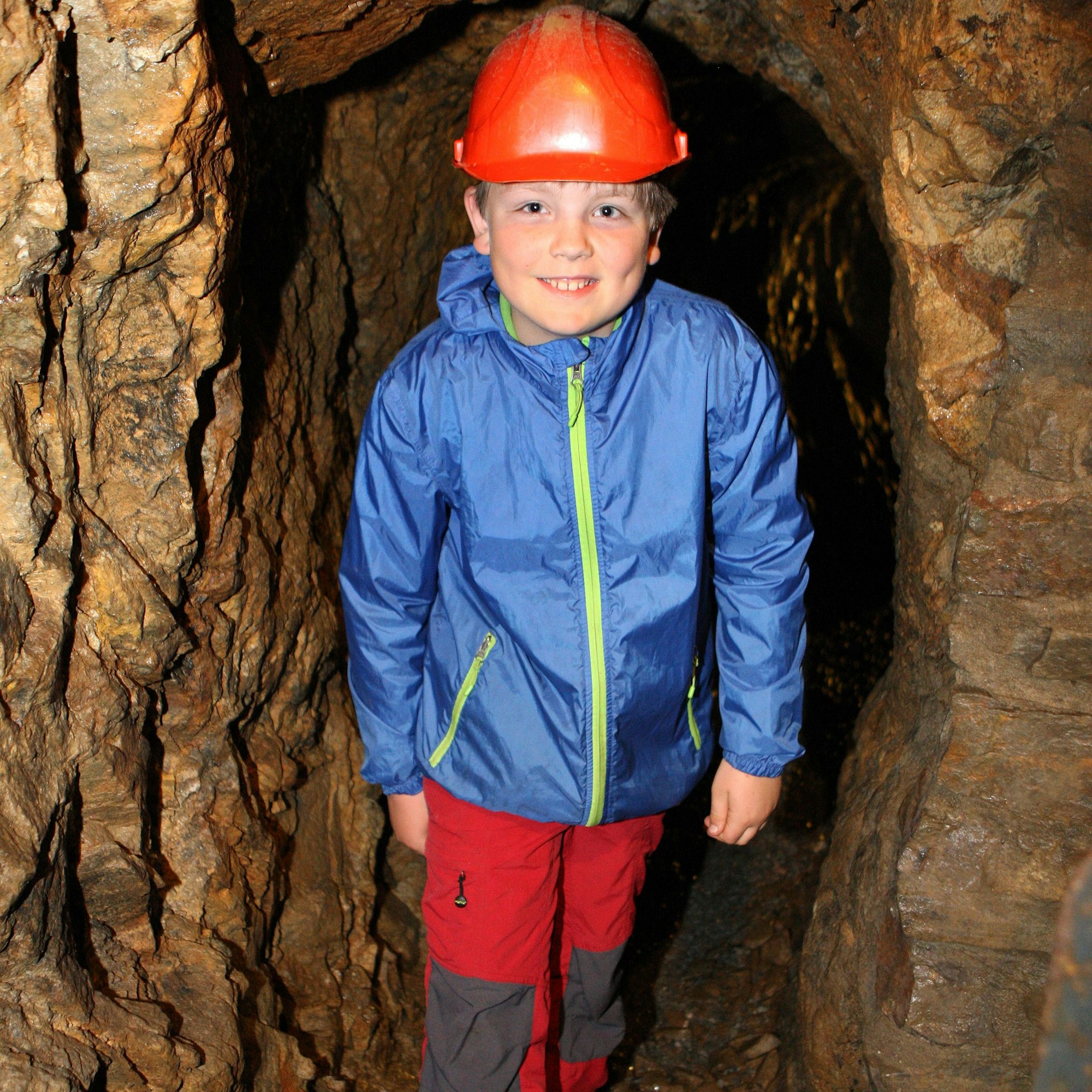 Ein Junge mit rotem Helm geht durch einen engen Bergwerksstollen.