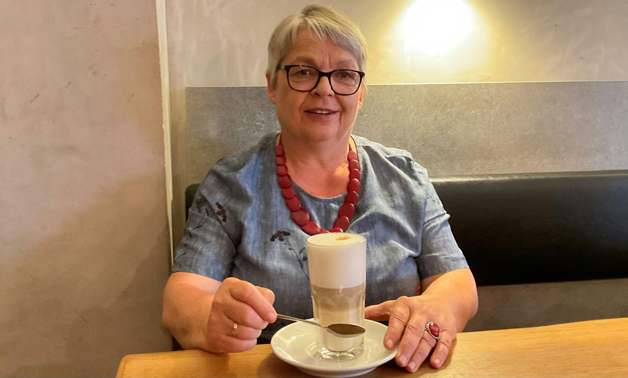 Grauhaarige Frau im Café mit Latte Macchiato