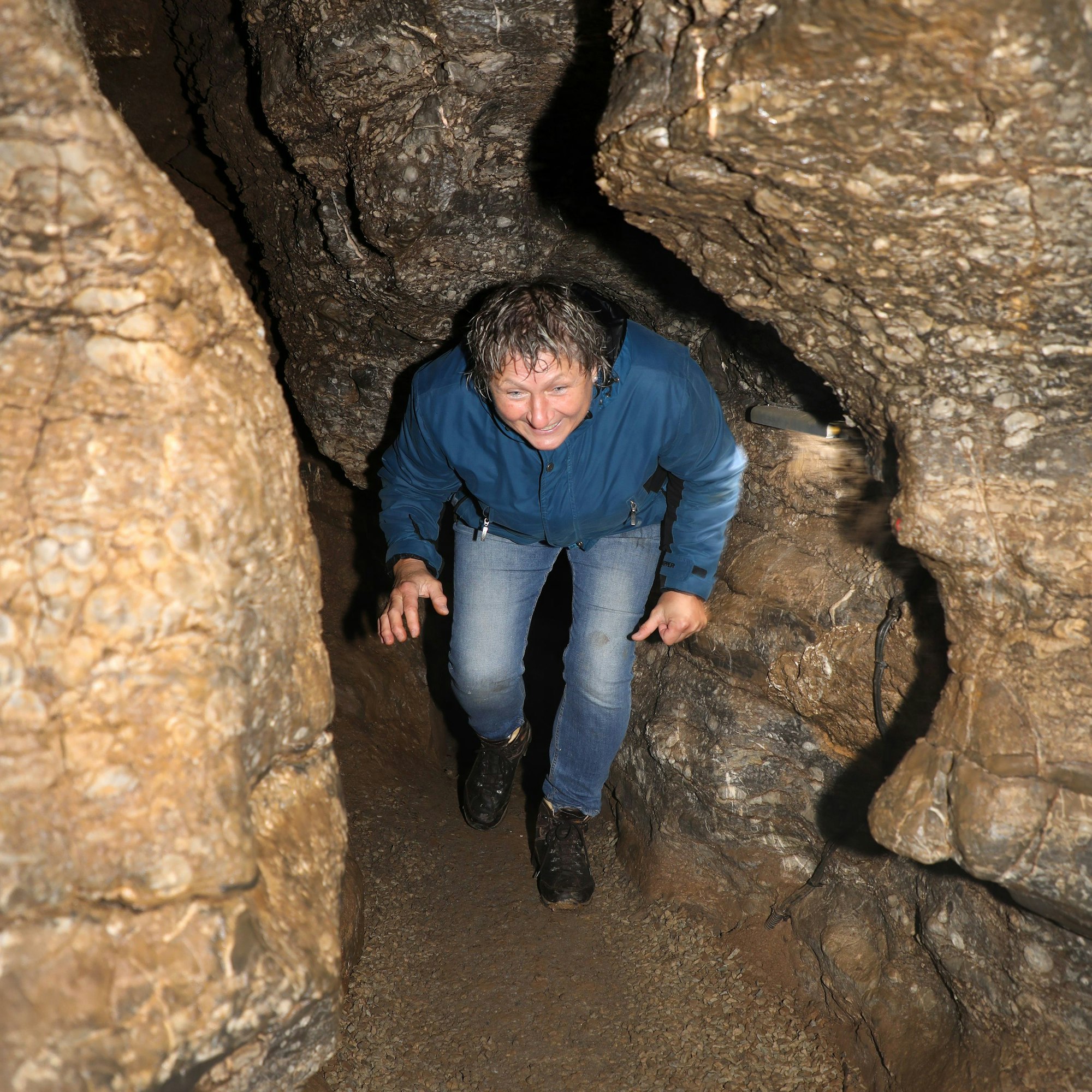 Eine Frau geht durch einen niedrigen Gang in der Aggertalhöhle.