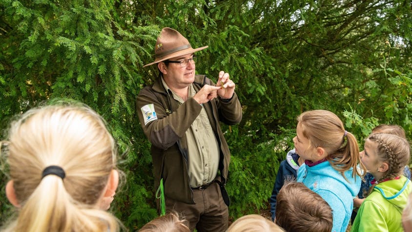 Ein Ranger des Nationalparks Eifel, der einen markanten braunen Hut trägt, erklärt Kindern Zusammenhänge aus der Natur