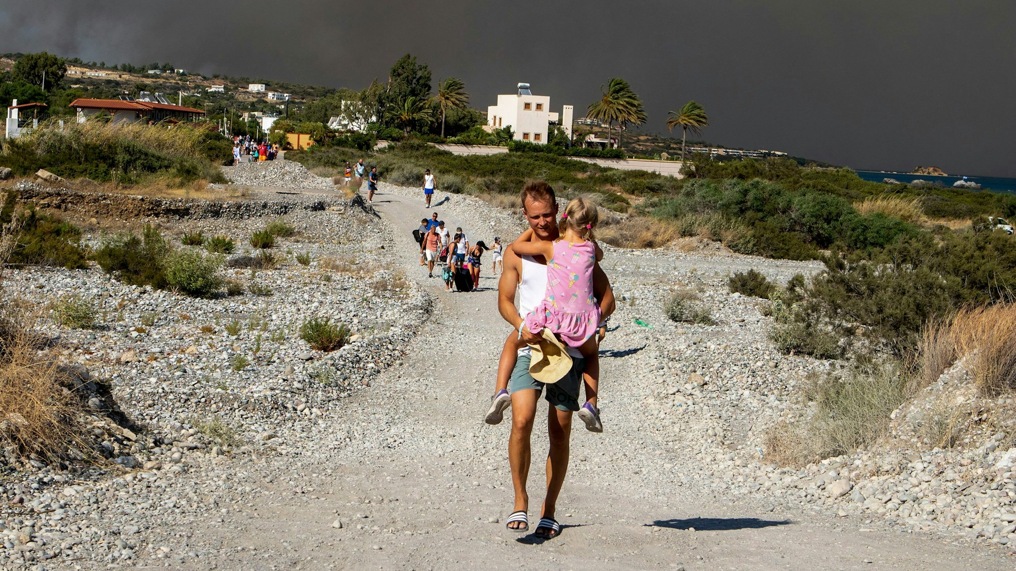 Ein Mann trägt ein Kind, als sie ein Waldbrandgebiet verlassen.