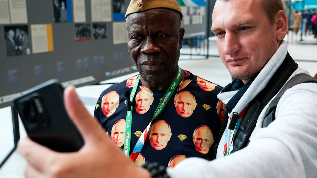 Lama Jacques Sevoba (l.), Botschaftsmitarbeiter aus Guinea, trägt ein T-Shirt mit Fotos des russischen Präsidenten Putin. Er sorgte mit seinem Outfit für Wirbel.