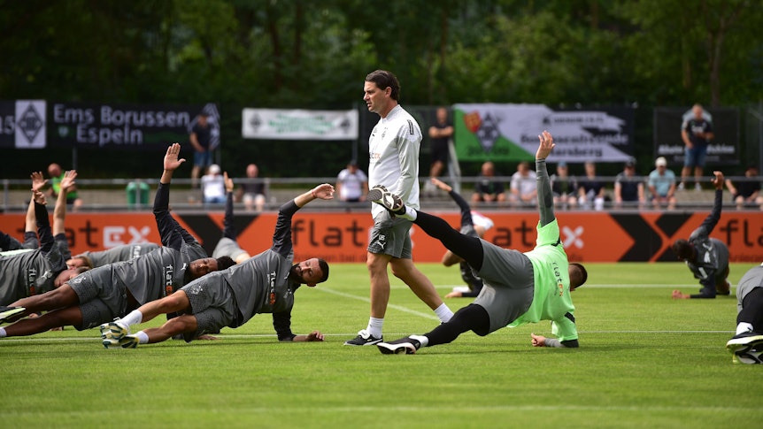 Gerardo Seoane steht bei einem Training von Borussia Mönchengladbach am 24. Juli 2023, während seine Spieler auf dem Rasen Stabilitäts-Übungen machen.