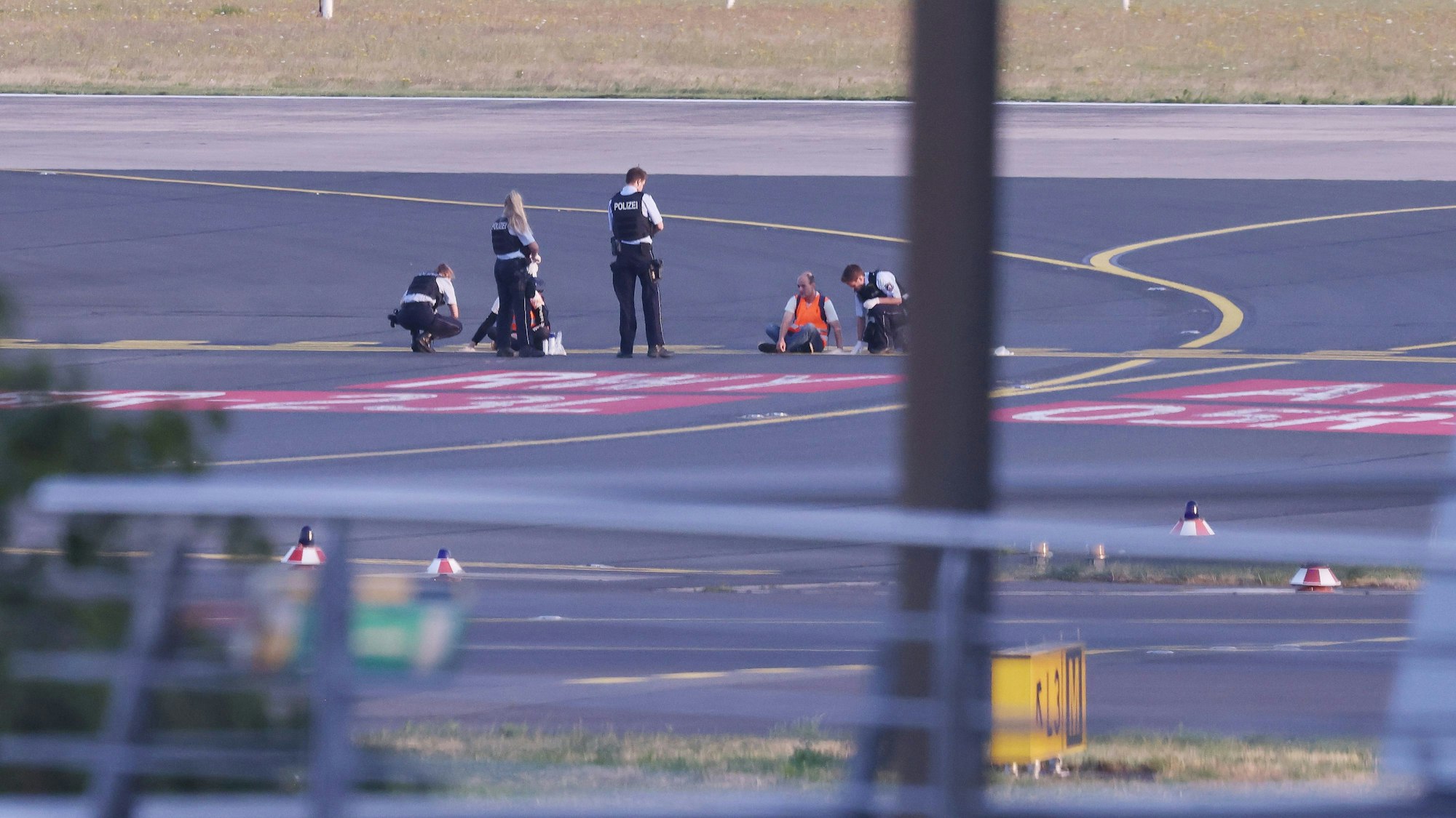 Düsseldorf: Polizisten stehen auf dem Flugfeld und versuchen Aktivisten der Gruppe Letzte Generation am Flughafen vom Asphalt zu lösen, nachdem diese sich festgeklebt hatten.