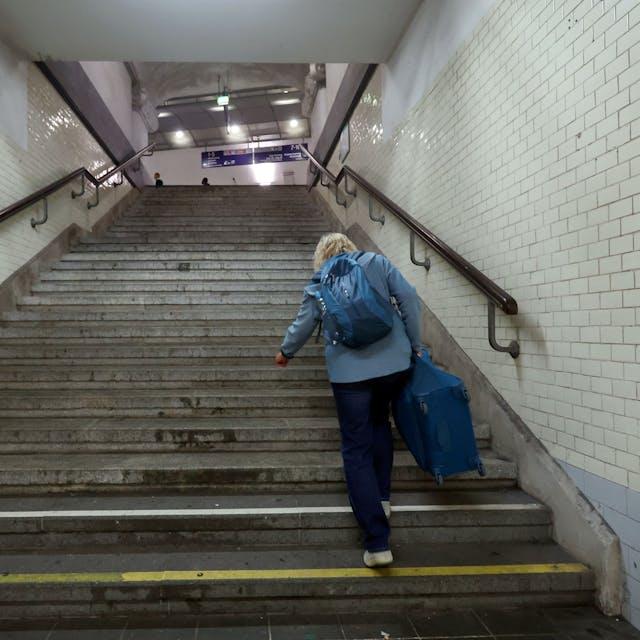 Eine Frau schleppt einen Koffer im Kölner Bahnhof Messe/Deutz über eine steile Treppe.