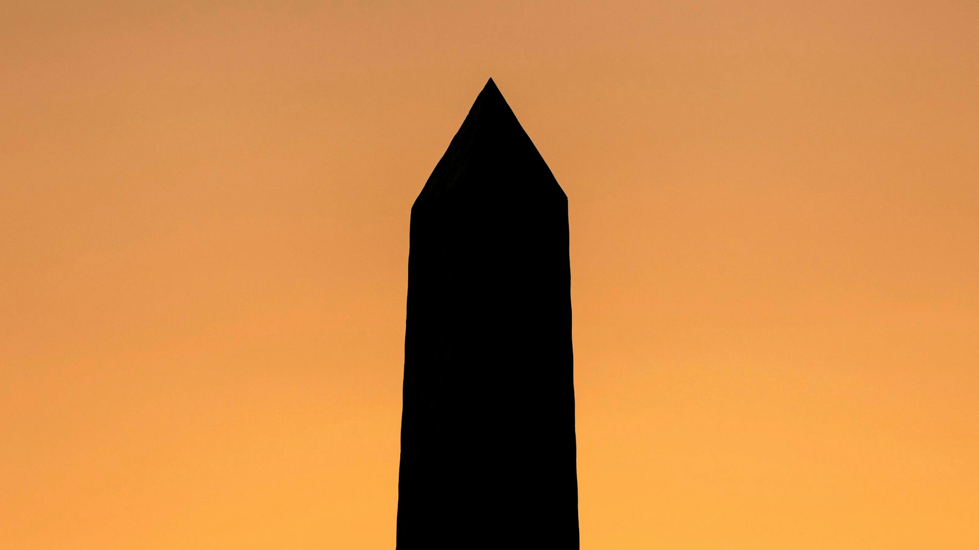 Die Spitze eines Obelisks steht schwarz vor einem orangefarbenen Himmel.